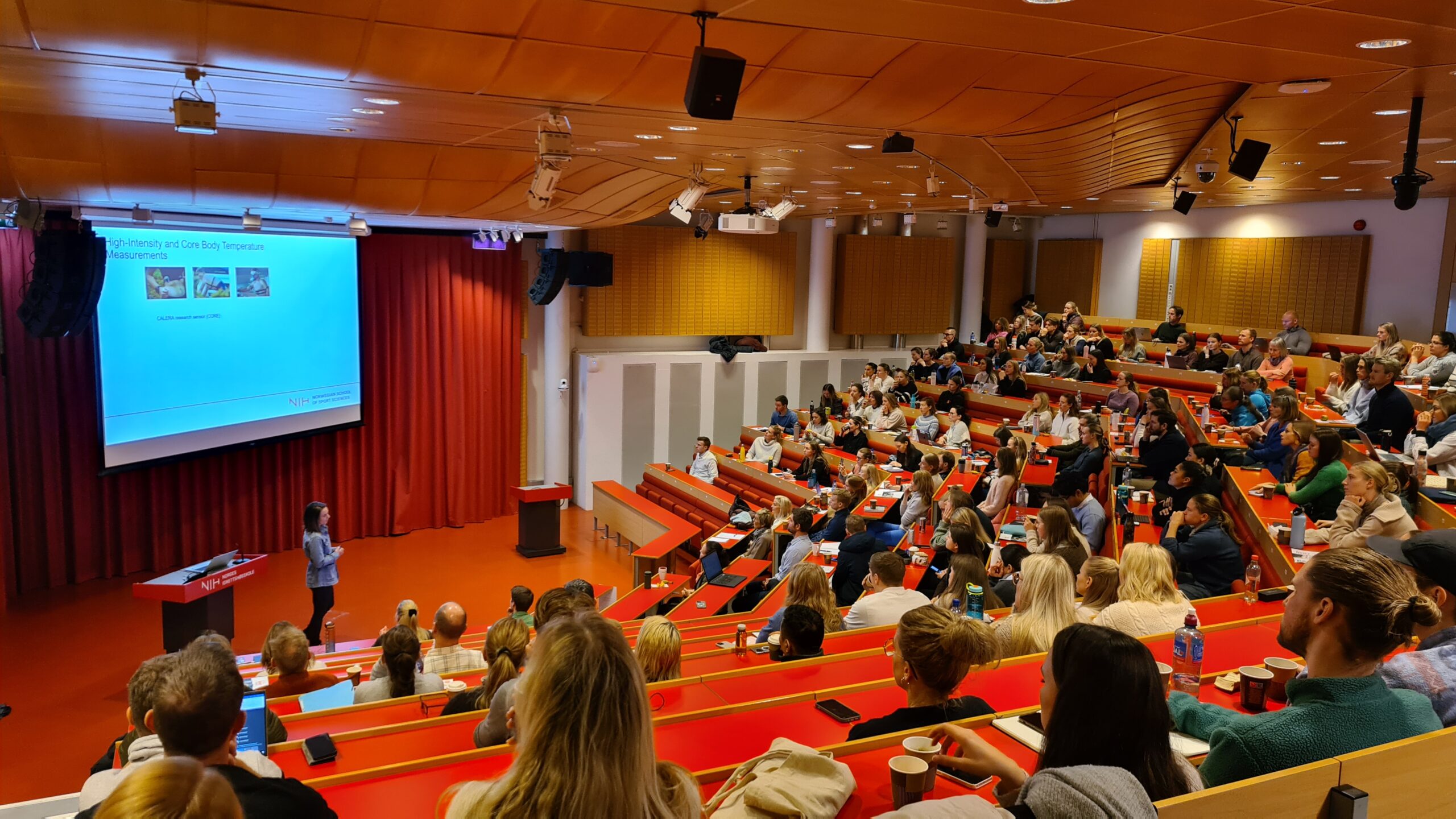 Oversiktsbilde av et auditorium med publikum og en konferansier